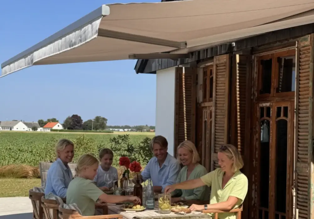 Utfälld terrassmarkis i sandfärgad väv över ett dukat matbord på en uteplats